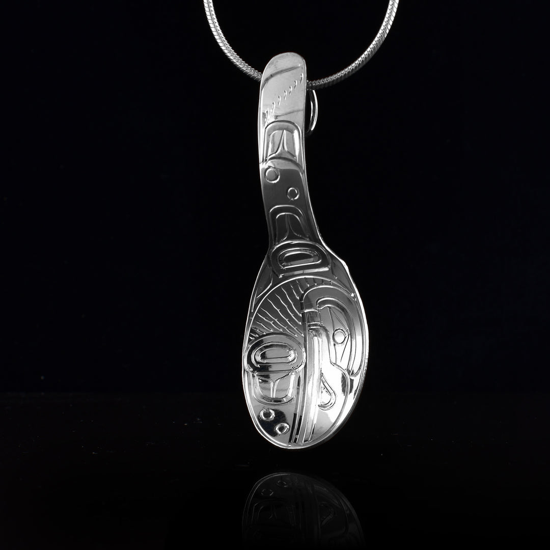This sterling silver Eagle pendant is shaped like a spoon and is attached by the end of the spoon's handle. The Raven legend is depicted in a side profile in the bowl of the spoon. Its beak is facing down and its wing is under it.