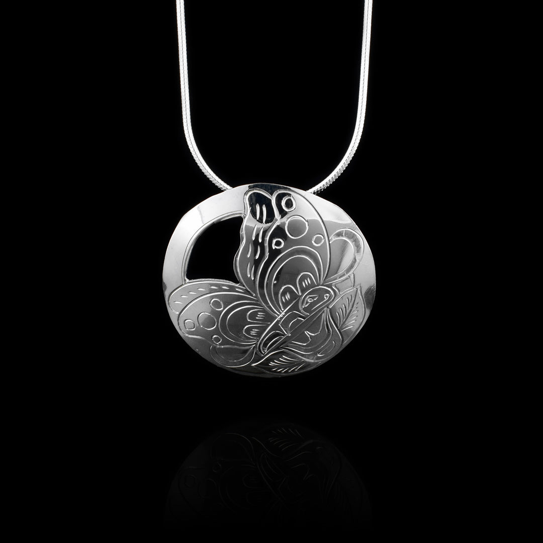 This butterfly pendant sterling silver has a circle shape and there is a depiction of the Butterfly resting on a flower carved into it. There are designs on the butterfly wings and the flower is at the bottom with two leaves coming out at the bottom. There is a cutout made around the wings at the top corner opposite of the flower.