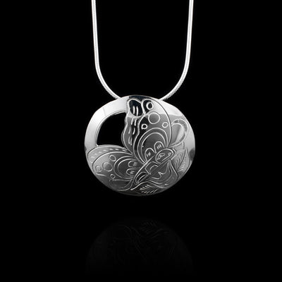 This butterfly pendant sterling silver has a circle shape and there is a depiction of the Butterfly resting on a flower carved into it. There are designs on the butterfly wings and the flower is at the bottom with two leaves coming out at the bottom. There is a cutout made around the wings at the top corner opposite of the flower.