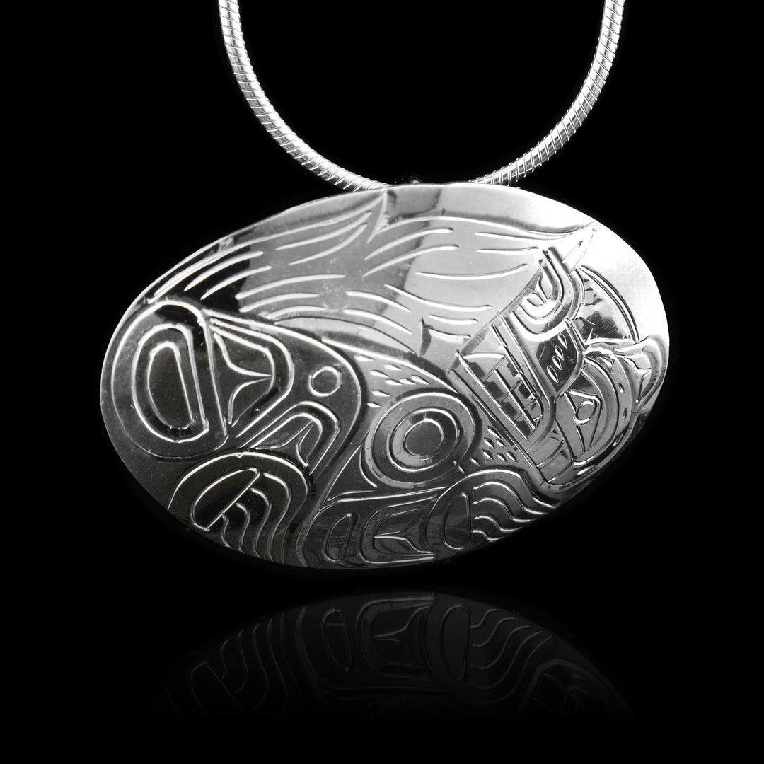 This Sterling silver Wolf pendant has a wide, oval shape with a depiction of the Wolf carved into it. The wolf is shown at a side profile and is curled up at the bottom of the piece with its tail tucked above it. Its head is looking up.