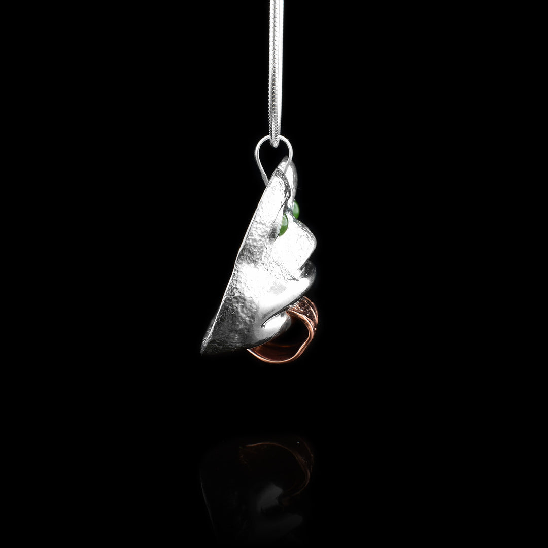 This Frog pendant depicts the face of the Frog which is done in sterling silver and has a copper band extending from the piece depicting its tongue. The eyes of the Frog are made from genuine BC jade. There are details carved onto the tongue and the face has been shaped with embossing.