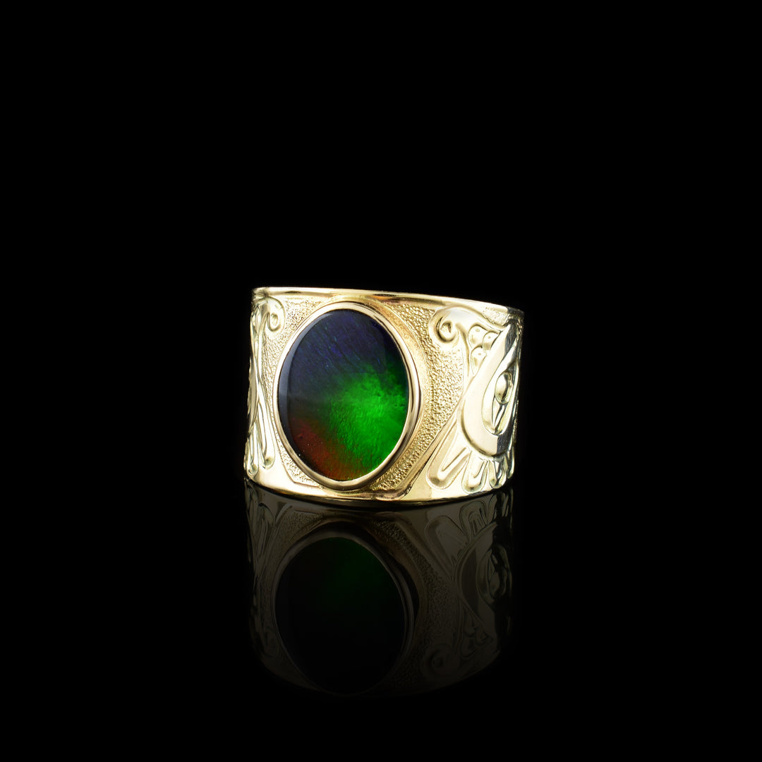 This 14K gold Thunderbird ring has a wide band with a depiction of the Thunderbird carved into the band. There is a large, circle shaped ammolite gem that makes up this large, signet ring.