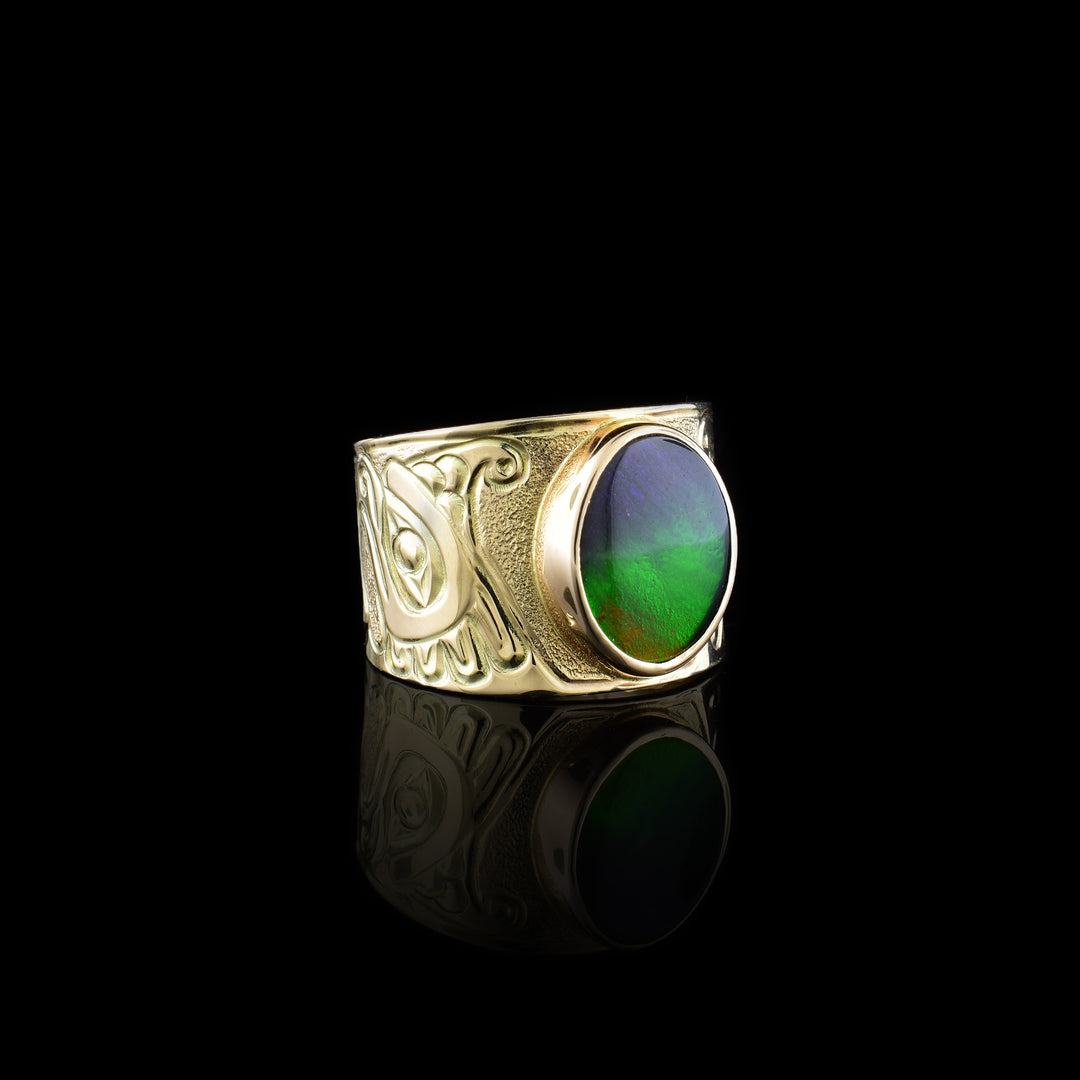 This 14K gold Thunderbird ring has a wide band with a depiction of the Thunderbird carved into the band. There is a large, circle shaped ammolite gem that makes up this large, signet ring.