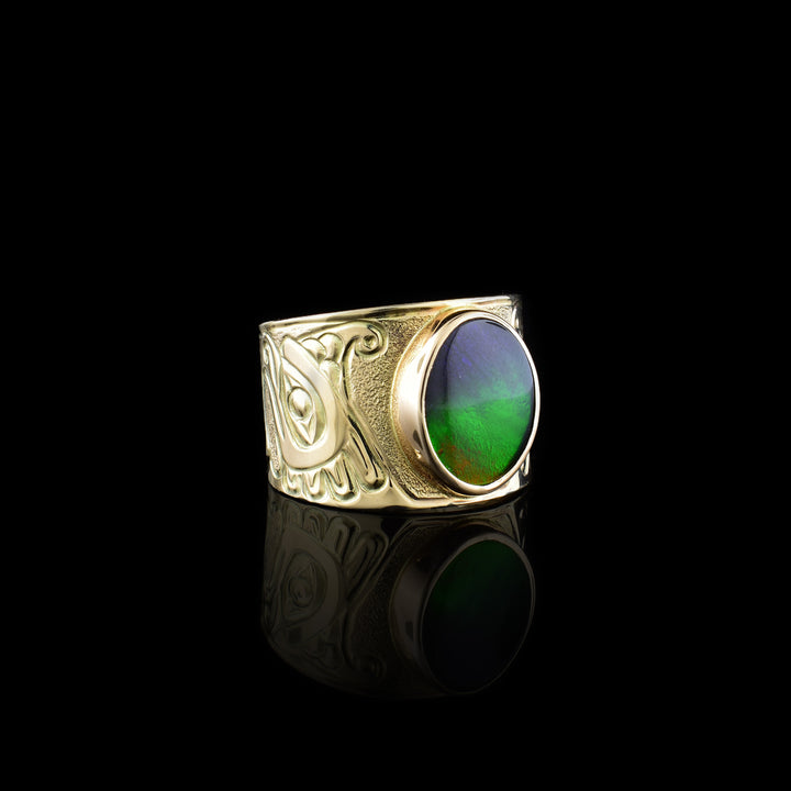 This 14K gold Thunderbird ring has a wide band with a depiction of the Thunderbird carved into the band. There is a large, circle shaped ammolite gem that makes up this large, signet ring.