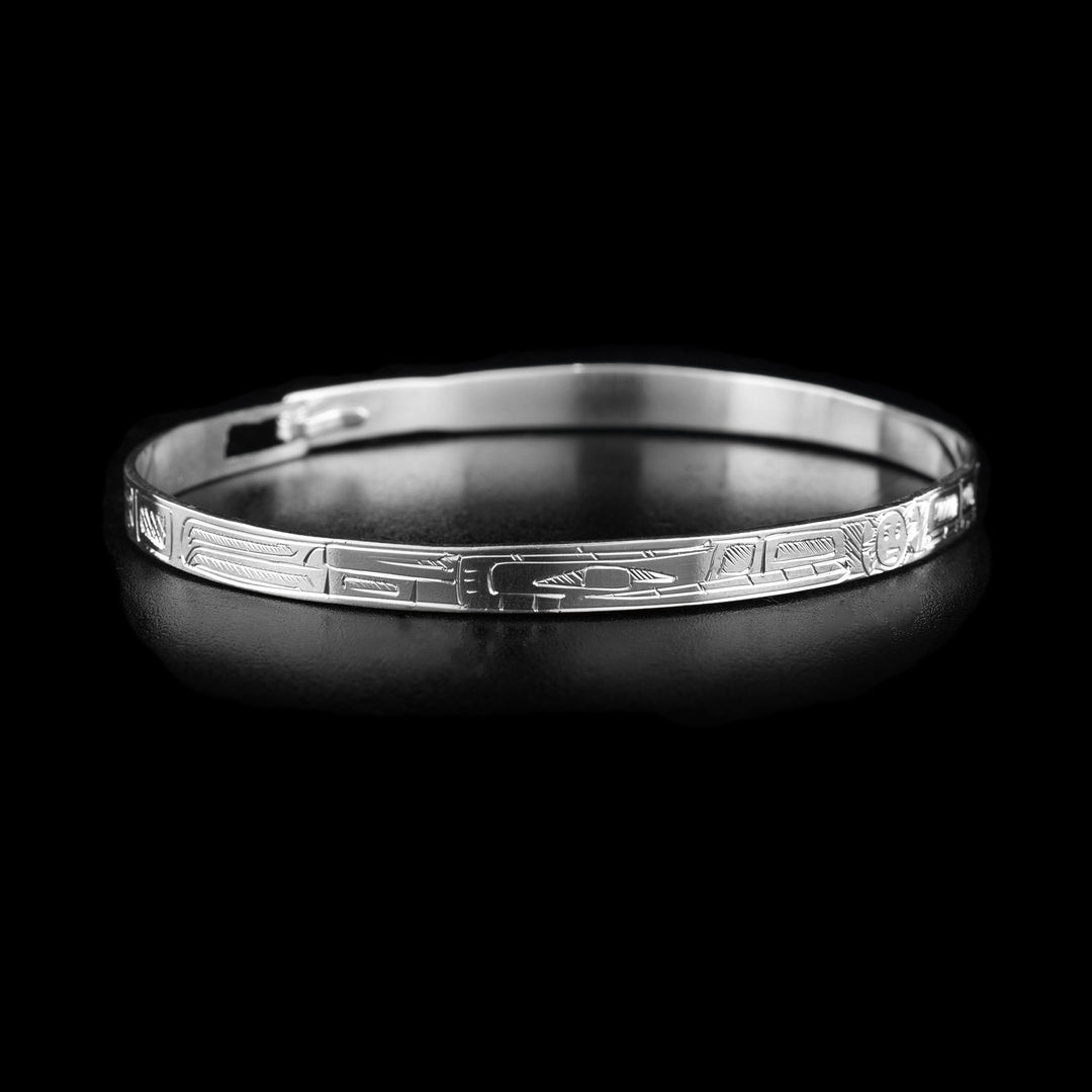 This thin bangle bracelet has a thin band made from sterling silver with a clasp in the back. There are carvings on the surface of the band showing two Wolves with their heads meeting at the front of the band. In between their heads, the moon is shown.