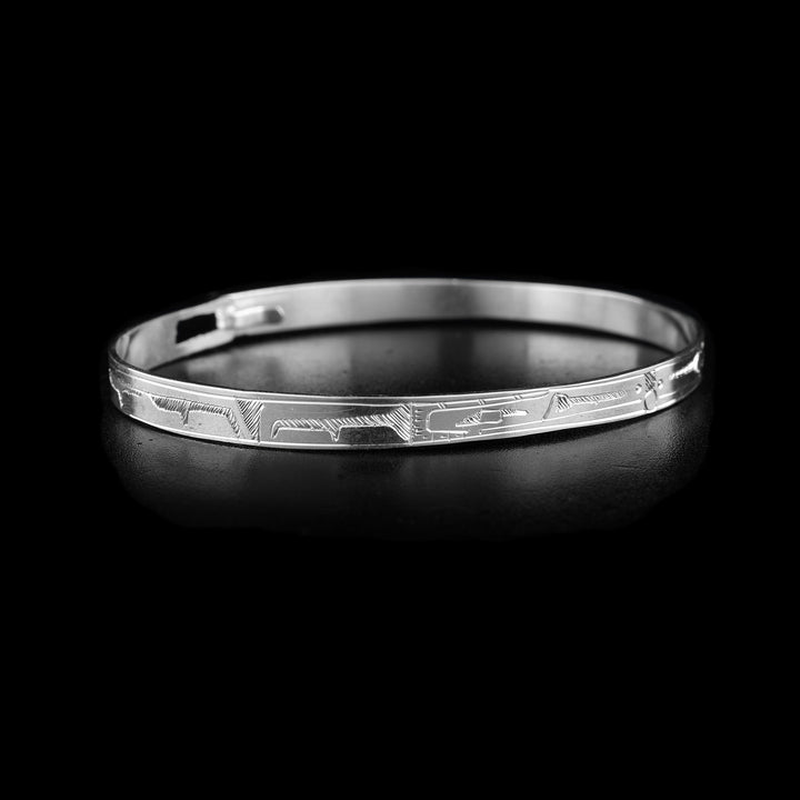 This thin bangle bracelet has a thin band made from sterling silver with a clasp in the back. There are carvings on the surface of the band showing two Ravens with their heads meeting at the front of the band. In between their heads, the Sun is shown.