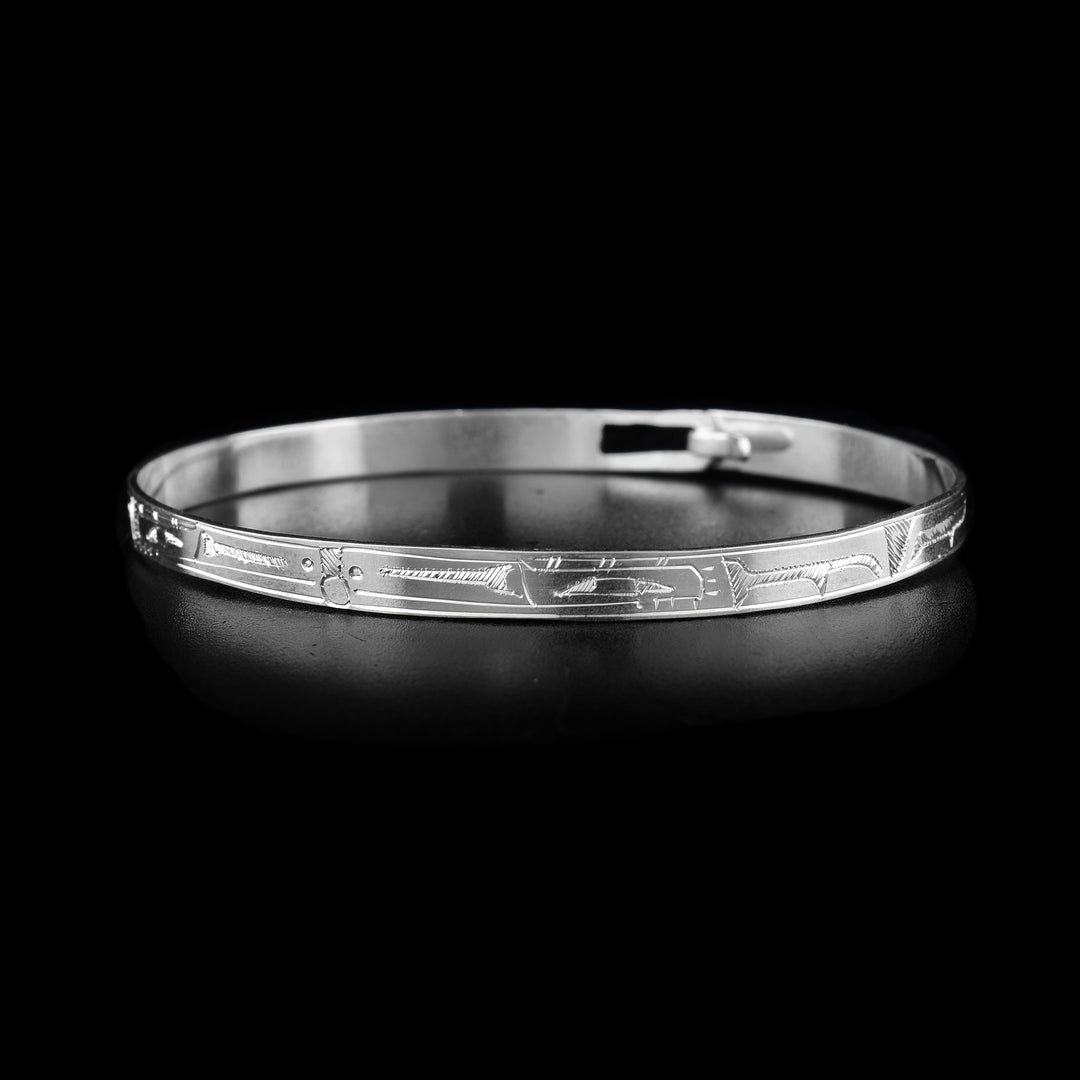 This thin bangle bracelet has a thin band made from sterling silver with a clasp in the back. There are carvings on the surface of the band showing two Ravens with their heads meeting at the front of the band. In between their heads, the Sun is shown.