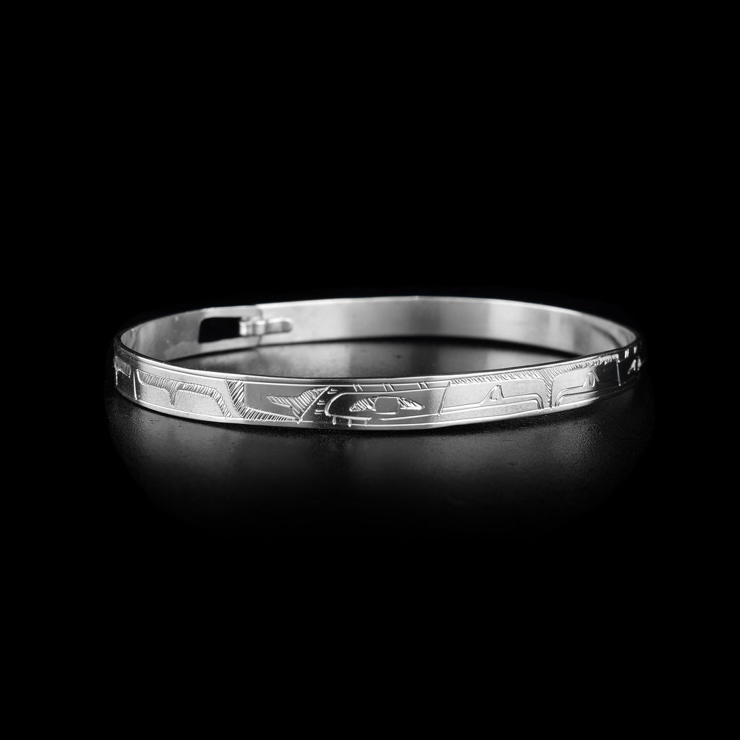 This sterling silver cuff bangle bracelet has a thin band with a clasp in the back. There are two Eagle legends carved into the surface of the band. Their heads meet at the front of the piece and their bodies extend around the rest of it.