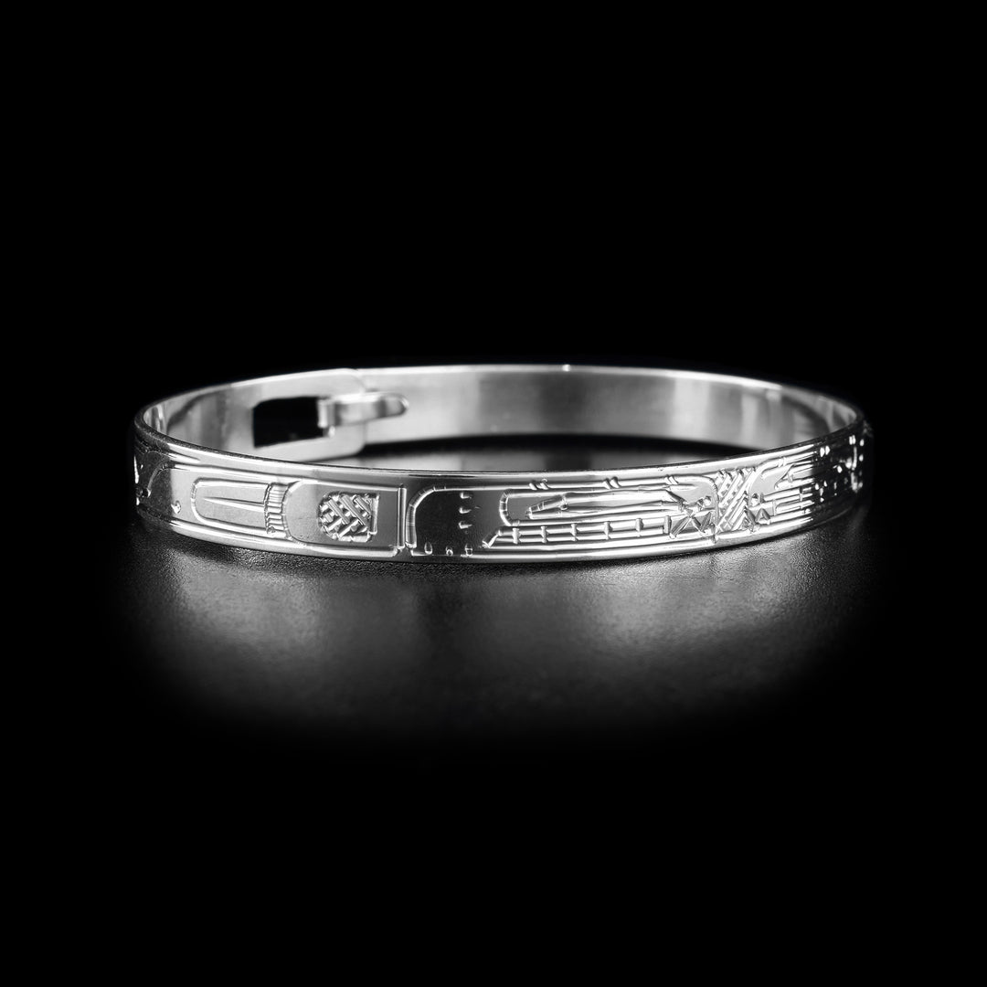 This sterling silver cuff bangle bracelet has a thin band with a clasp in the back. There are two Orca legends carved into the surface of the band. Their heads meet at the front of the piece and their bodies extend around the rest of it.
