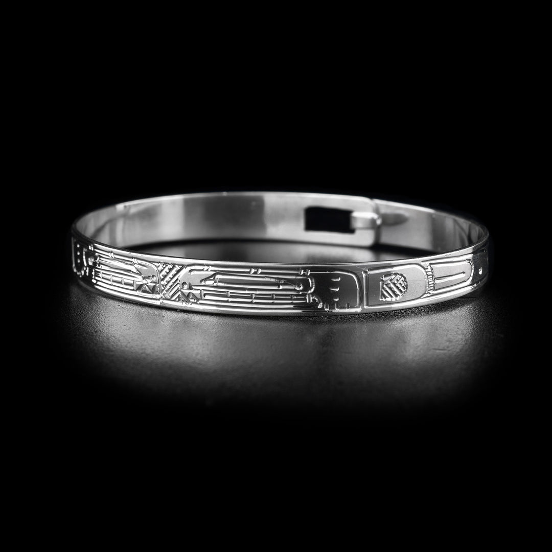This sterling silver cuff bangle bracelet has a thin band with a clasp in the back. There are two Orca legends carved into the surface of the band. Their heads meet at the front of the piece and their bodies extend around the rest of it.