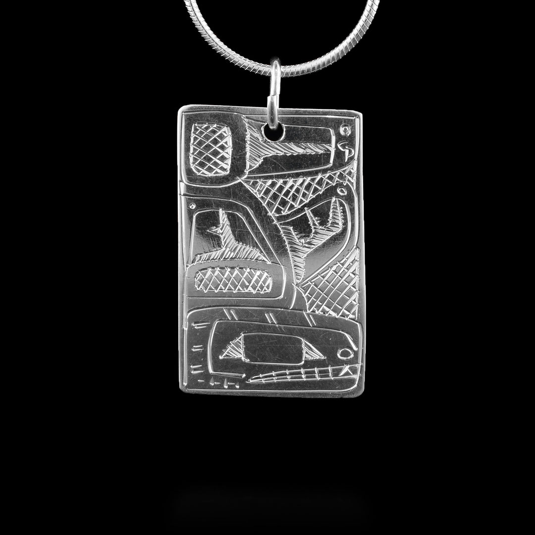 This Orca pendant has a wide, rectangle shape and is made from sterling silver. The Orca is depicted on both sides of the piece with its head at the bottom and the rest of its body running up the side and across the top. There are details showing its eye, teeth and designs on the fins and tail. There are cross hatching patterns in the negative spaces of the scene.
