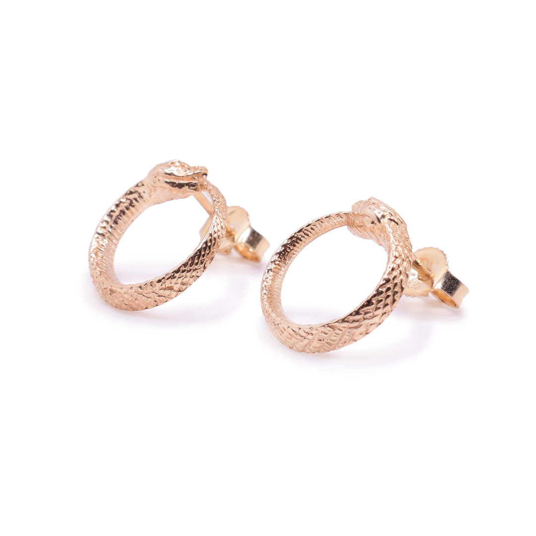 These ouroboros earrings are made from 10K gold and are circle shaped. The studs are attached to the tops of the circles and they look like snakes with their tails curled up into their mouths. There are scale details on the studs and they have detail heads.