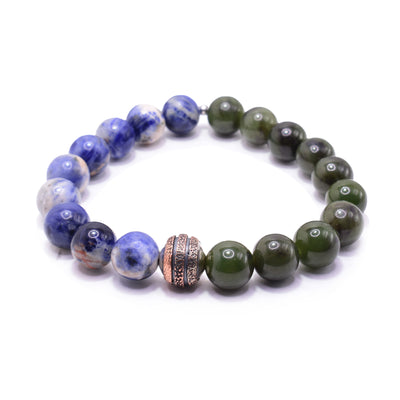 This jade charm bracelet has small, sphere shaped beads made from sodalite and BC jade. The sodalite is multi colored with white and purple designs. Half the piece is jade and the other is sodalite. there is a copper charm bead in the center of the piece with textured bands going around it.