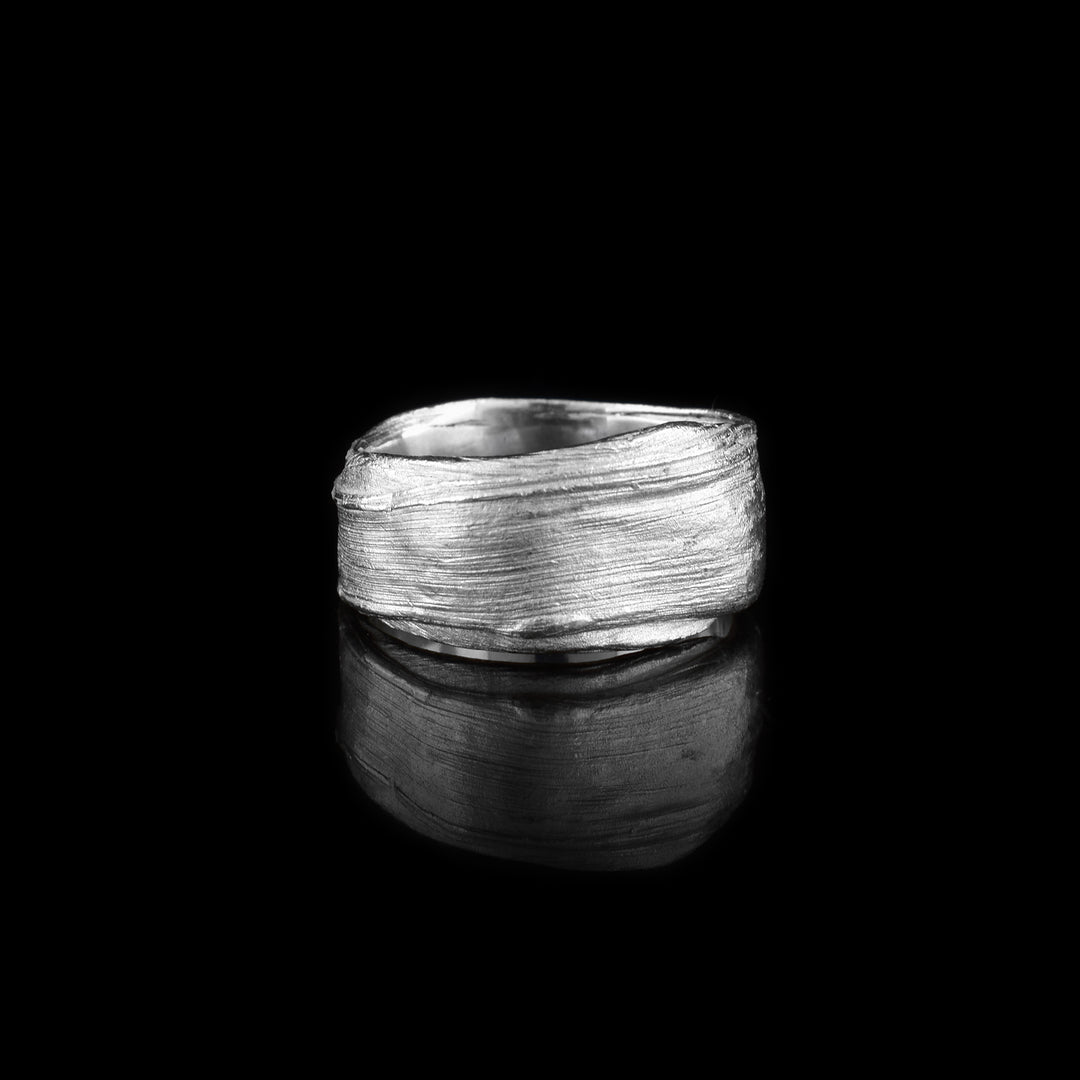 This wide silver band ring is made from sterling silver and has flowing designs on the surface of it. The piece is made by casting metal into wax so it mimics the appearance of it wax mold. The ring is chunky and has a large gauge.