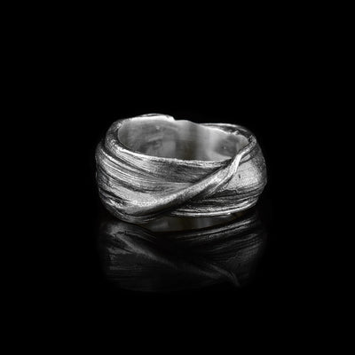 This wide silver band ring is made from sterling silver and has flowing designs on the surface of it. The piece is made by casting metal into wax so it mimics the appearance of it wax mold and has a vein running diagonally across the band. The ring is chunky and has a large gauge.