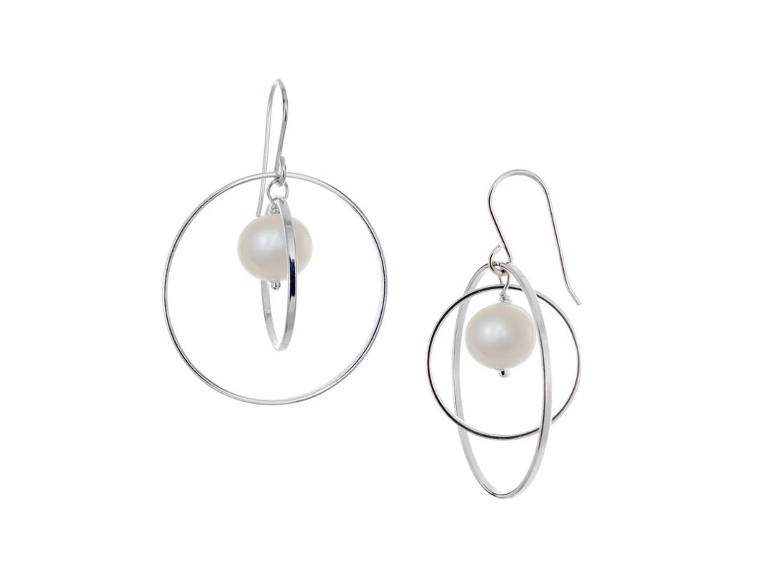 These hoop dangle earrings have large, sterling silver hoops with a smaller one inside of it. In the middle is a sphere shaped white pearl bead. All of these pieces are dangling and fit inside each other. The hoops are free to orbit around the gem.