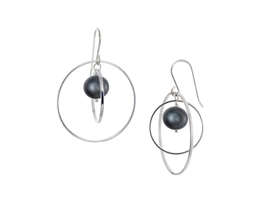 These hoop dangle earrings have large, sterling silver hoops with a smaller one inside of it. In the middle is a sphere shaped black pearl bead. All of these pieces are dangling and fit inside each other. The hoops are free to orbit around the gem.