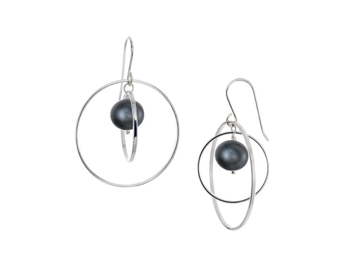 These hoop dangle earrings have large, sterling silver hoops with a smaller one inside of it. In the middle is a sphere shaped black pearl bead. All of these pieces are dangling and fit inside each other. The hoops are free to orbit around the gem.