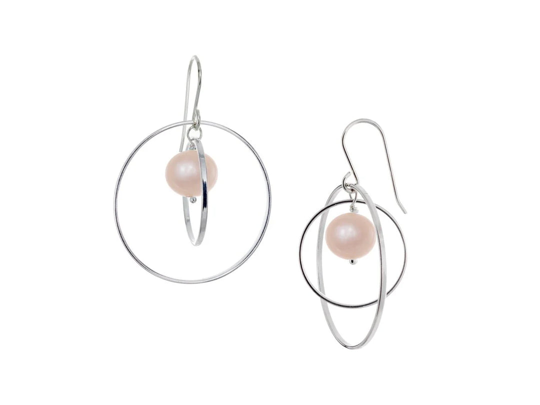 These hoop dangle earrings have large, sterling silver hoops with a smaller one inside of it. In the middle is a sphere shaped pink pearl bead. All of these pieces are dangling and fit inside each other. The hoops are free to orbit around the gem.