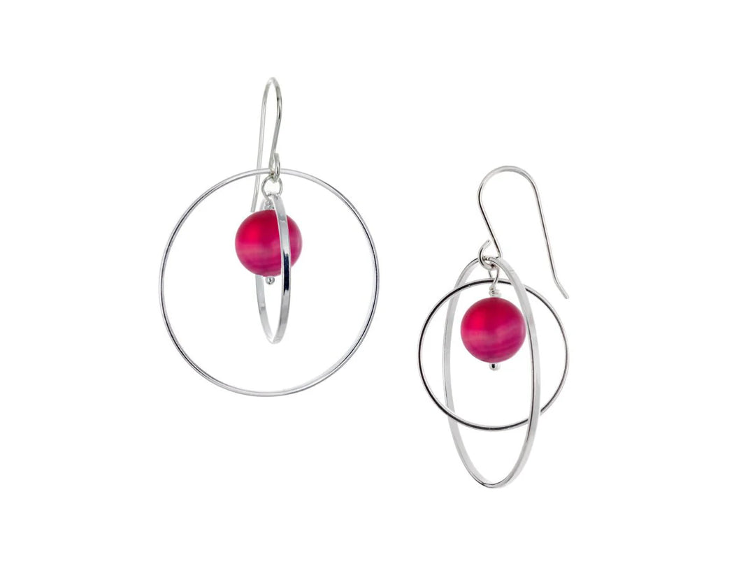 These hoop dangle earrings have large, sterling silver hoops with a smaller one inside of it. In the middle is a sphere shaped pink agate bead. All of these pieces are dangling and fit inside each other. The hoops are free to orbit around the gem.