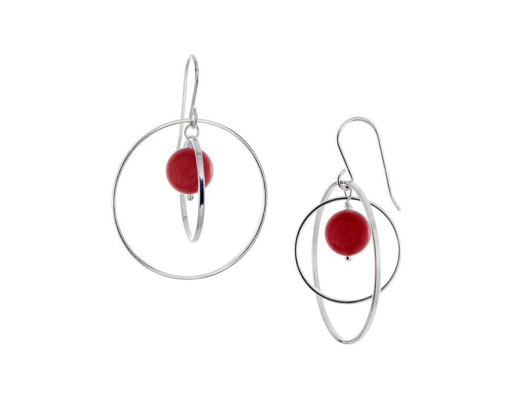 These hoop dangle earrings have large, sterling silver hoops with a smaller one inside of it. In the middle is a sphere shaped red bamboo coral bead. All of these pieces are dangling and fit inside each other. The hoops are free to orbit around the gem.
