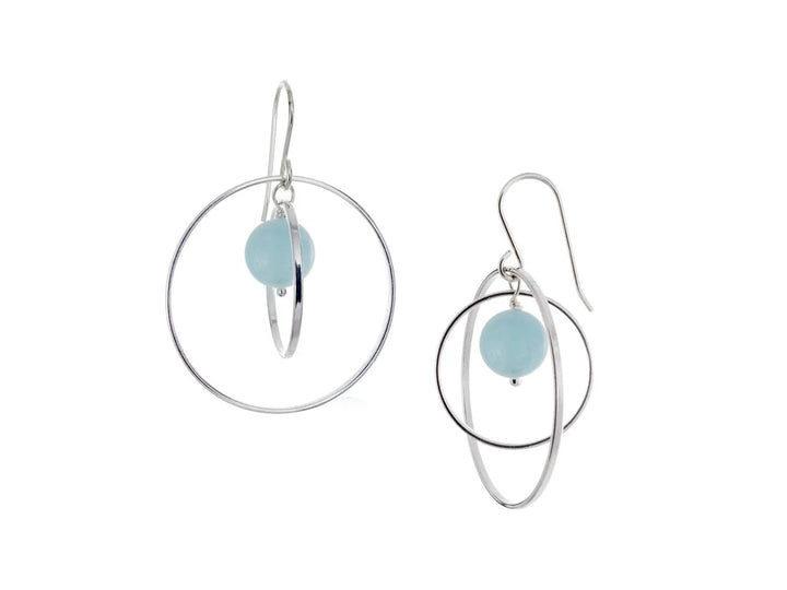 These hoop dangle earrings have large, sterling silver hoops with a smaller one inside of it. In the middle is a sphere shaped aquamarine bead. All of these pieces are dangling and fit inside each other. The hoops are free to orbit around the gem.