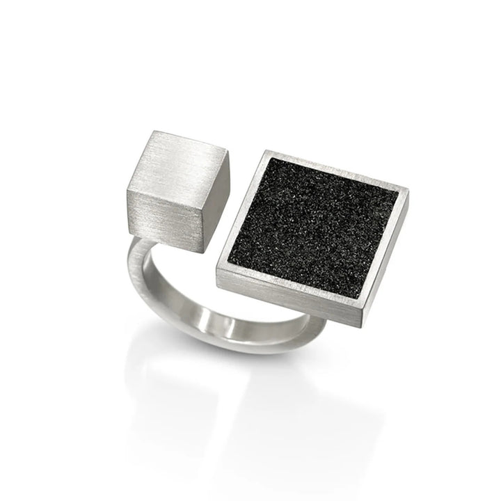 This stainless steel ring has two main centerpieces. The larger one is flat, square-shaped and features the black-tinted concrete and diamond dust. Right beside it is a stainless steel cube half the size. Both are independetly connected to the band.