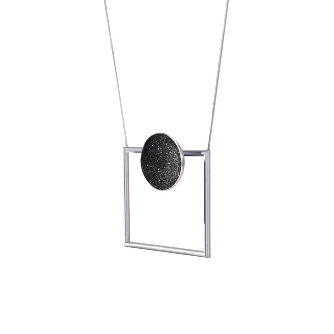 This stainless steel necklace features a large, hollow square-shaped frame to which the chain is attached to. Attached to the top bar of the square is a domed circle with concrete and diamond dust finish.