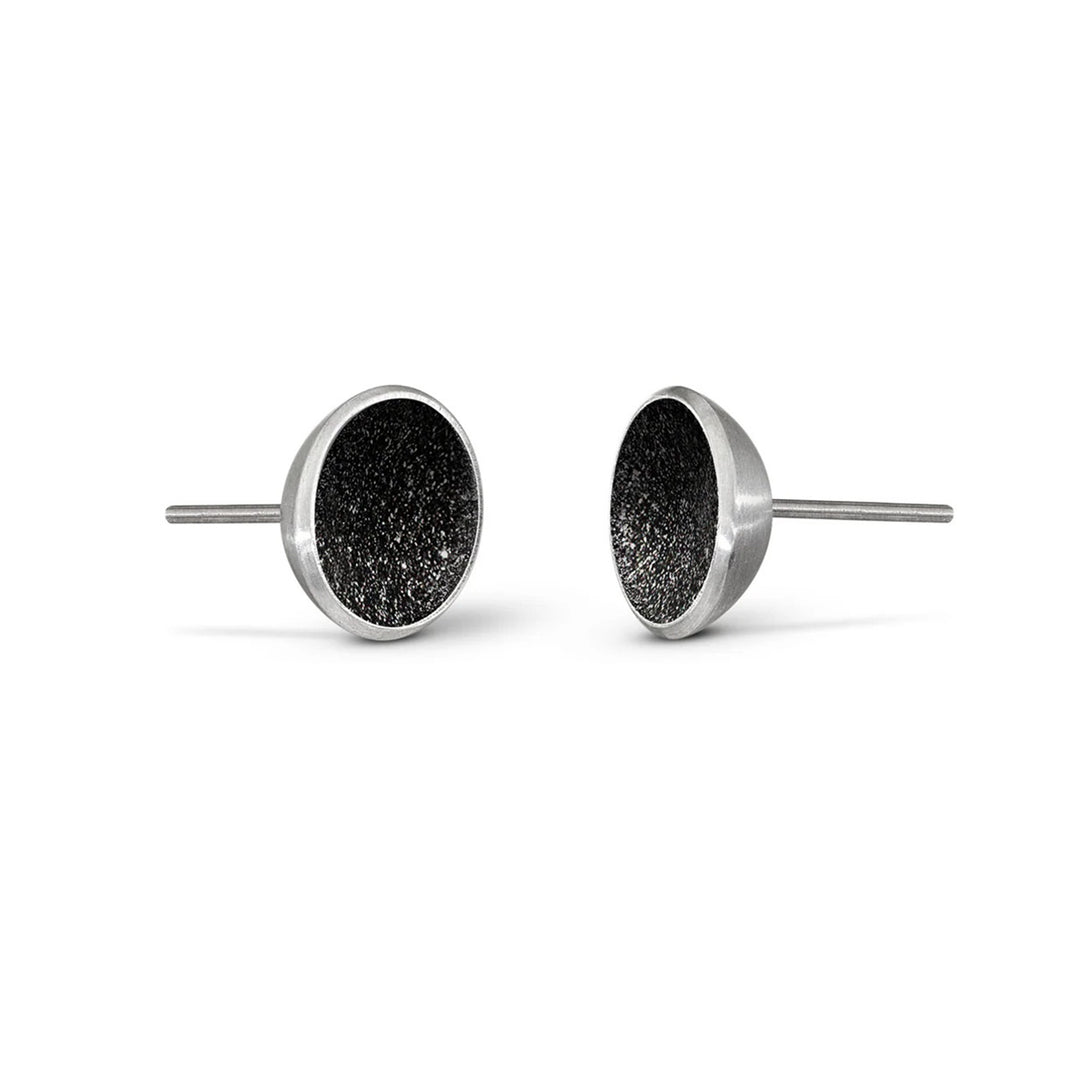 These stainless steel stud earrings feature a round centerpiece made from black concrete with diamond dust helping it shine. The small border encasing the concrete is stainless steel.