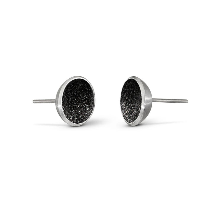 These stainless steel stud earrings feature a round centerpiece made from black concrete with diamond dust helping it shine. The small border encasing the concrete is stainless steel.