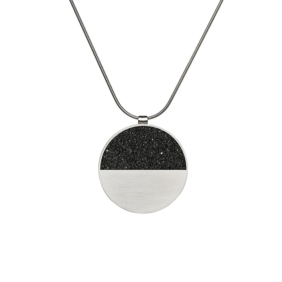 This stainless steel necklace is circular in shape with the top half black and shiny from diamond dust and the bottom half stainless steel. The bail is at the top of the round pendant.
