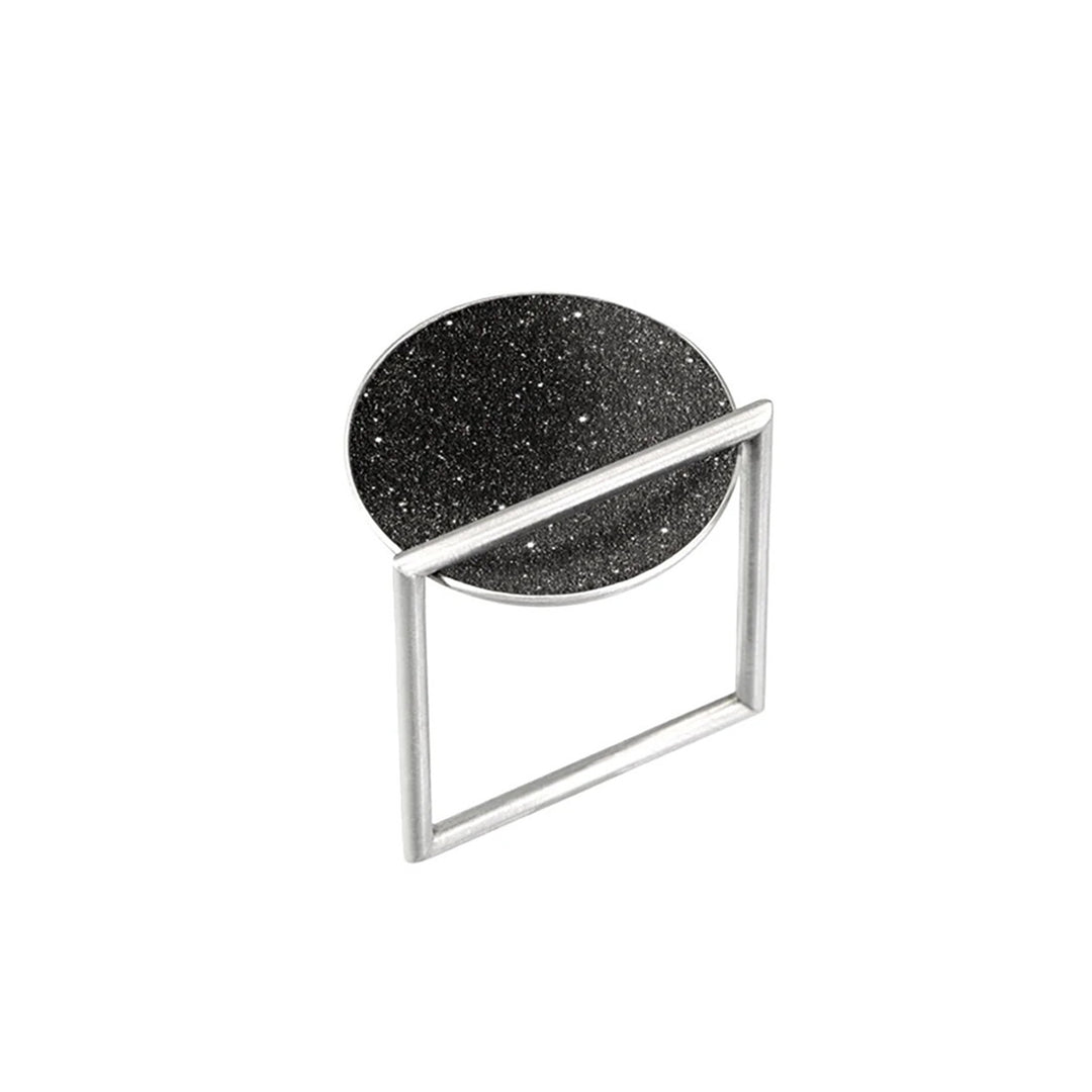 This stainless steel ring has a unique square-shaped, thin band with a round bowl-shaped centerpiece with black-tinted concrete and diamond dust on top.