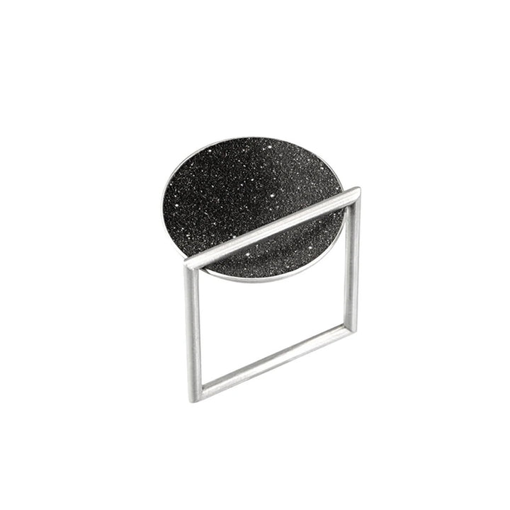 This stainless steel ring has a unique square-shaped, thin band with a round bowl-shaped centerpiece with black-tinted concrete and diamond dust on top.