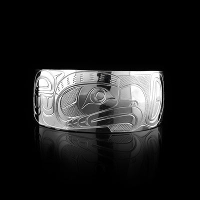This bracelet for baby has a single, wide band with a gap in the back that is made from sterling silver. The Thunderbird legend is carved at a side profile across the band. The head is large and in the centre of the band. On either side of the head, there are designs representing wings with individual feather details. There are cross hatching designs made in the negative space of the scene.