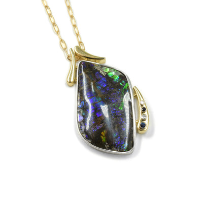 This ammolite pendant las 14K gold teardrops at the top of the piece that act as the bail. There is a large, oblong teardrop shaped ammolite piece that is held around sterling silver and is the main part of the piece. At the bottom side of the ammolite is a long, gold teardrop shape that has two diamonds and two sapphires embedded into it.