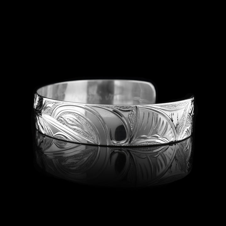This Hummingbird flower bracelet has a single band with a gap in the back and is made from sterling silver. There are depictions of the Hummingbird legends done in a side profile. There is a flower in the center of the piece and a Hummingbird on either side of the flower. There are dimpled designs in spaces of the scene to give contrast.