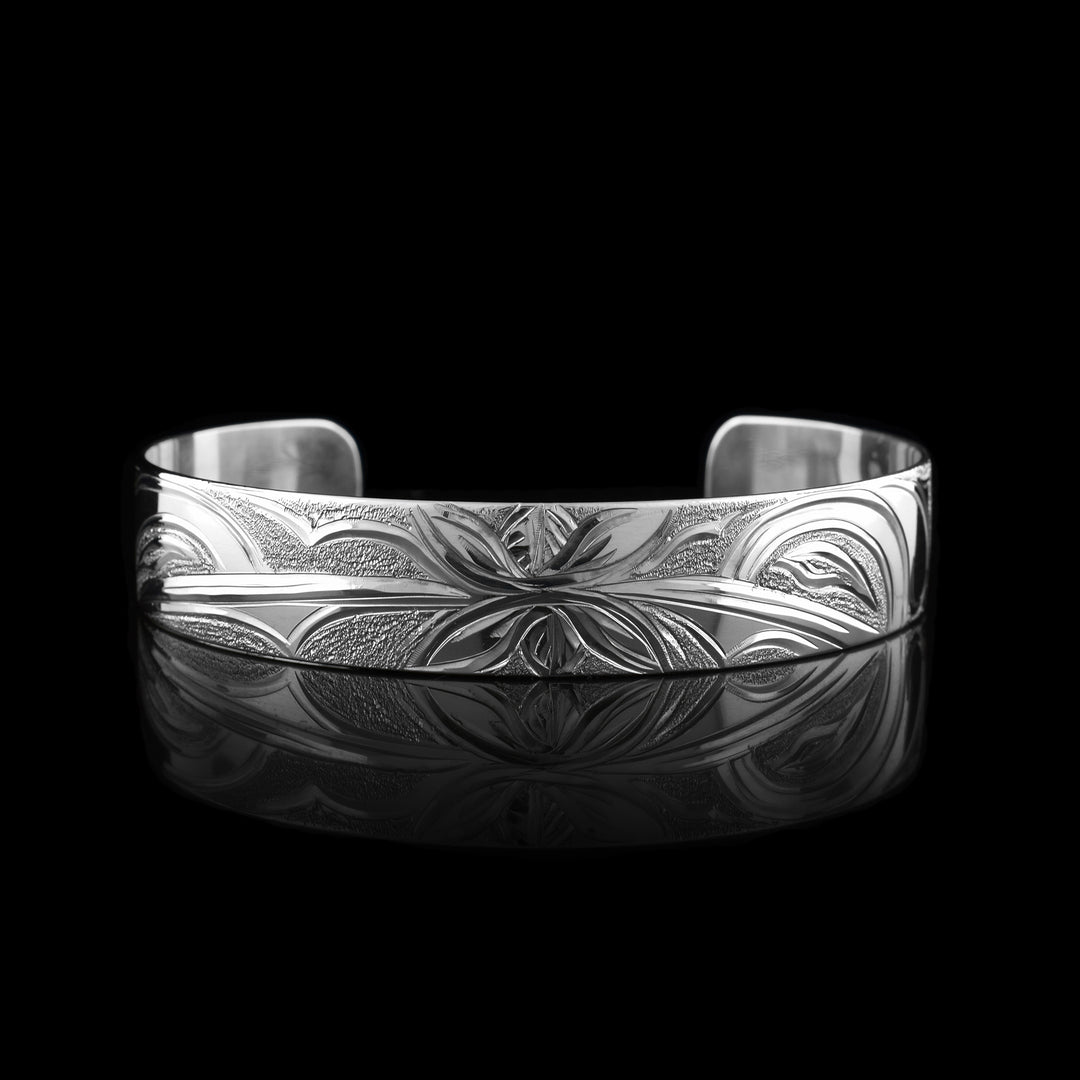This Hummingbird flower bracelet has a single band with a gap in the back and is made from sterling silver. There are depictions of the Hummingbird legends done in a side profile. There is a flower in the center of the piece and a Hummingbird on either side of the flower. There are dimpled designs in spaces of the scene to give contrast.