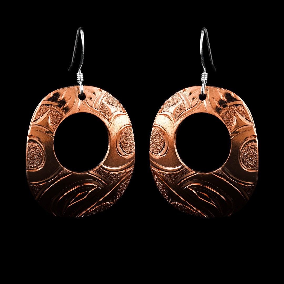 These Hummingbird earrings have oval shaped hangs made from copper. The hangs are wide ovals with small cutouts in the center of them. The head of the Hummingbird is carved into the bottom of the hangs and there are flower designs on the rest of the piece. There are small, dimpled textures in the negative spaces of the scene.