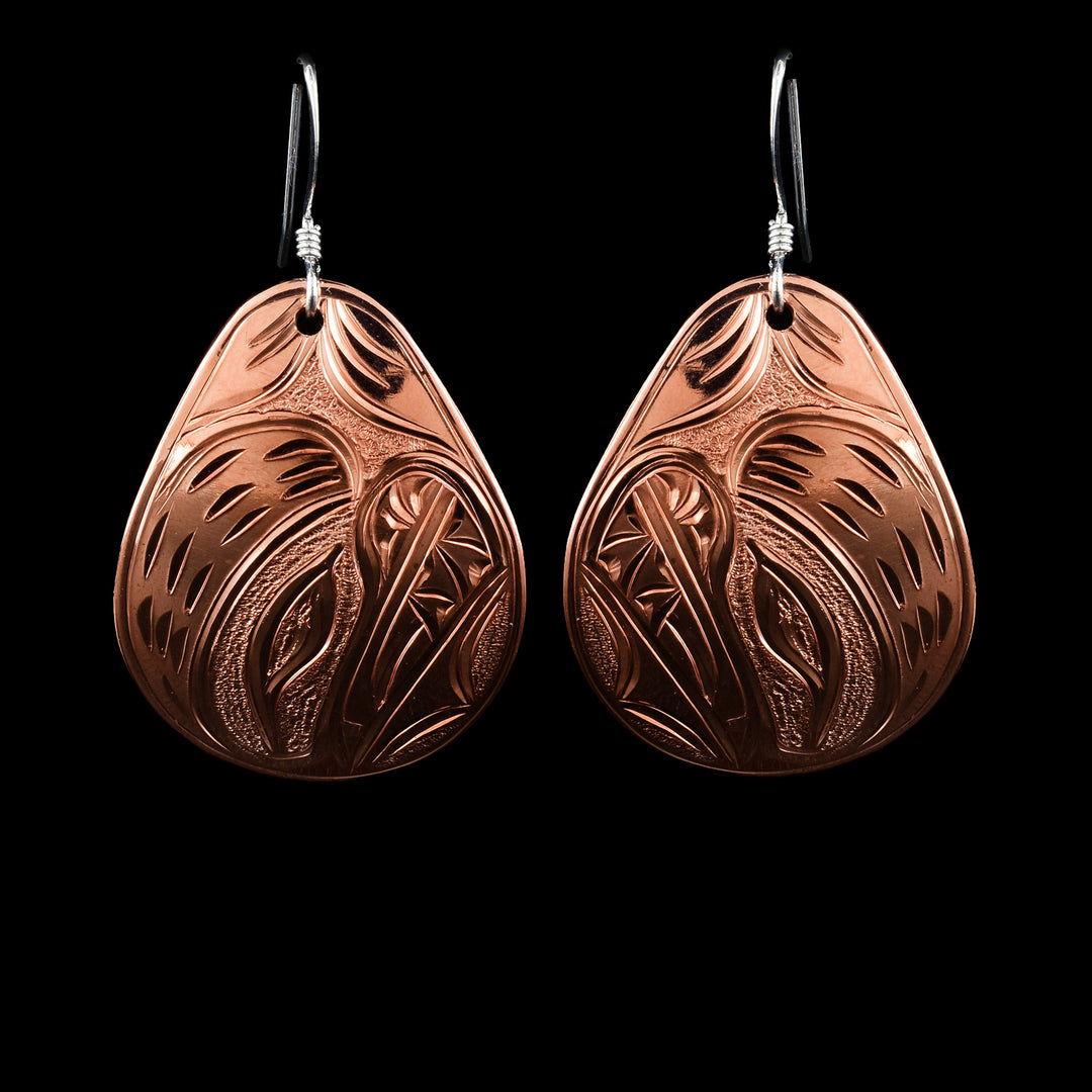 These Bear earrings have large, wide and teardrop shaped hangs made from copper. The head of the Bear legend is large and carved into the center of the hangs. The head is looking up and the eye, teeth, mouth, and nose are detailed.