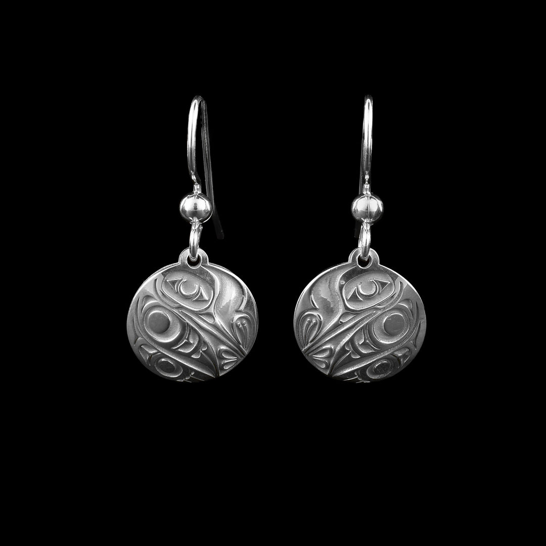 These sterling silver Hummingbird earrings have small, circle hangs with a depiction of the Hummingbird legend made in the surface of them. The legend is done in a side profile with its head at the top and its beak facing downwards into a flower on the other side. Its wing and tail go  cross the bottom of the hangs.