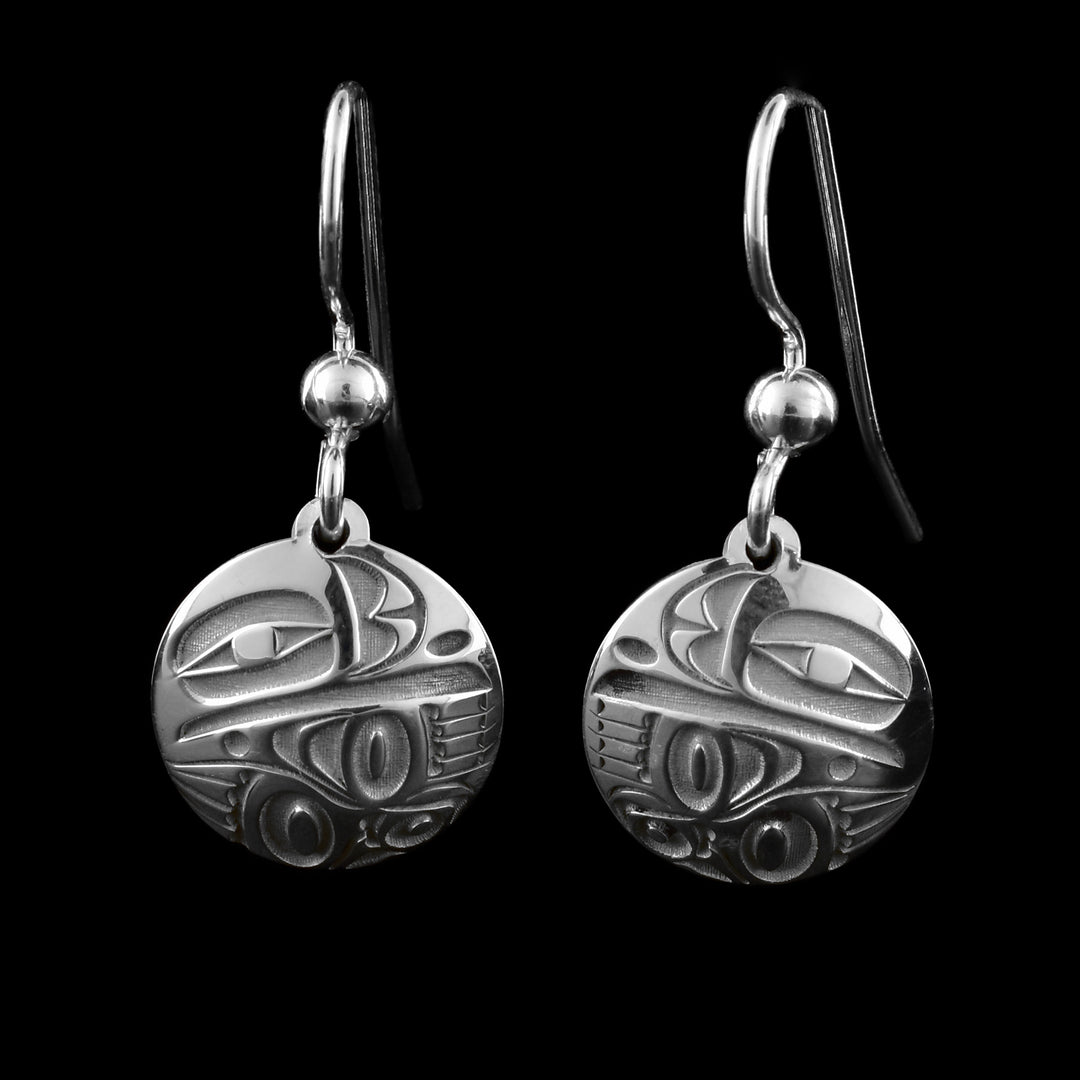 These Raven silver earrings have small, circle hangs made from sterling silver. a depiction of the Raven legend is made on the hangs with its eye and beak at the top. The wings are at the bottom and wrap around the length of the hangs.