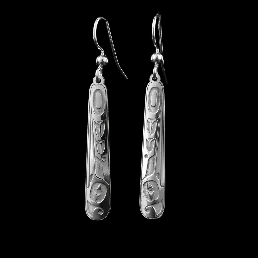 These long drop earrings silver have long, thin hangs with round edges. The hangs are made from sterling silver and are slightly wide at the bottom than the top. The Hummingbird legend is depicted in the surface of them. Its head is show at the bottom with its beak going up the side of the piece. One of its wings is designed on the other side of the hangs.