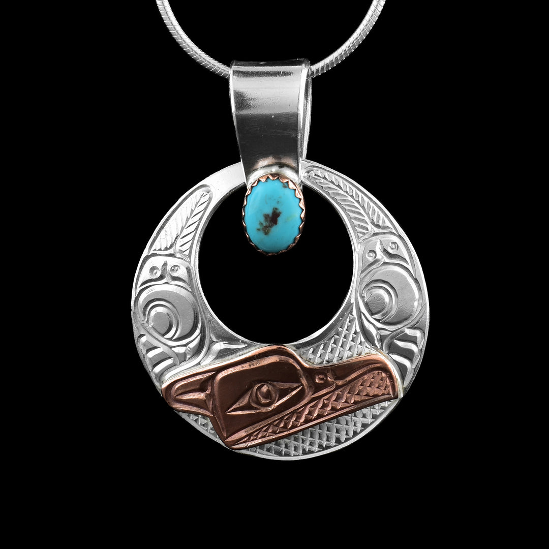 This turquoise pendant has a sterling silver circle with a circle cutout in the center of it. The head of the Raven is done in the bottom using copper and the details of the head are carved into it. The wings extend up on both sides of the piece.