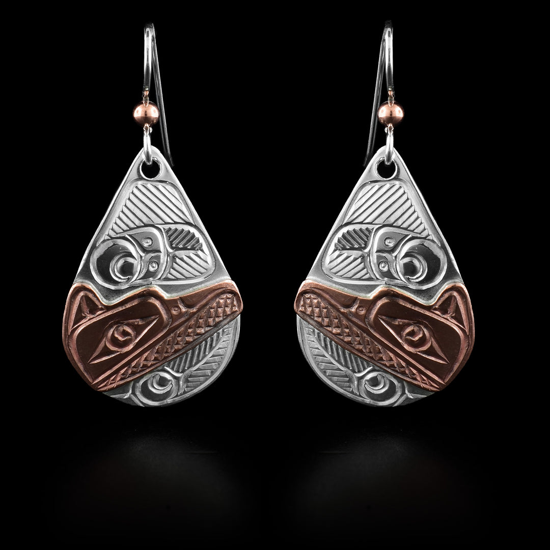 These Raven earrings have a wide, teardrop shape and are made from sterling silver and copper. The head of the Raven is done in copper and the details are carved into the hangs. Around the head, there are feather designs carved into the silver.