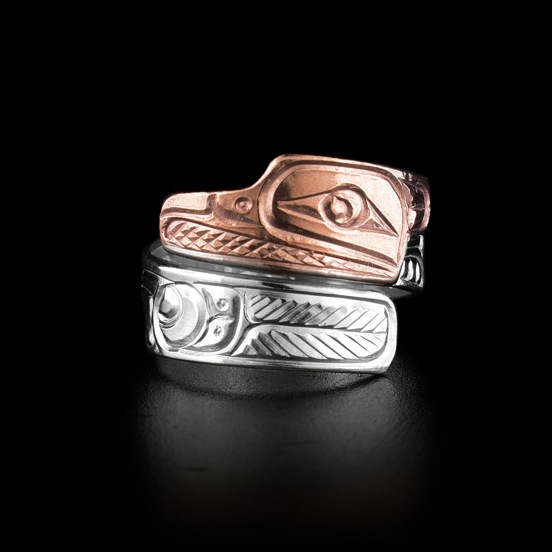 This sterling silver and copper ring has a single band that wraps around the finger twice. The end of the top band its done in copper and shaped like the head of the Raven. There are details carved into the band showing the face of the raven and the bottom band has feather details representing the wing of the Raven.