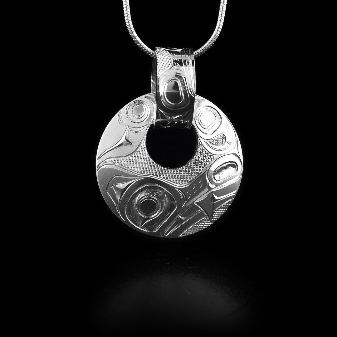 This sterling silver Wolf pendant has a circle shape with a small, circle cutout close to the top of the piece. There is a wide, decorative bail linked through the cutout with a depiction of the Wolf and designs carved into it. The head of the Wolf is depicted at a side profile at the bottom of the pendant and designs representing its leg and tail across the rest.
