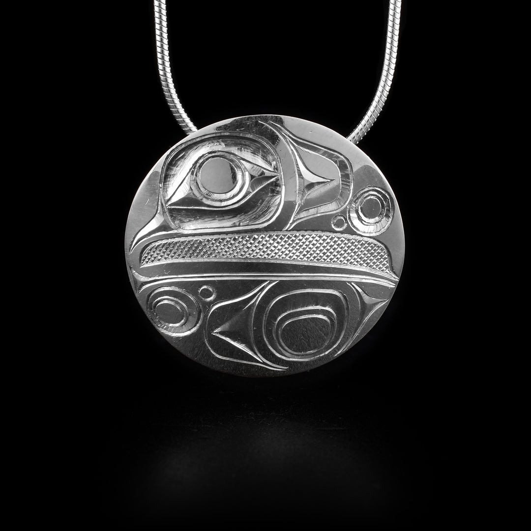 This sterling silver Raven pendant has a circle shaped and has carvings depicting the Raven legend. The head of the Raven is shown at the top half with its large eye and beak and below is a wing design.