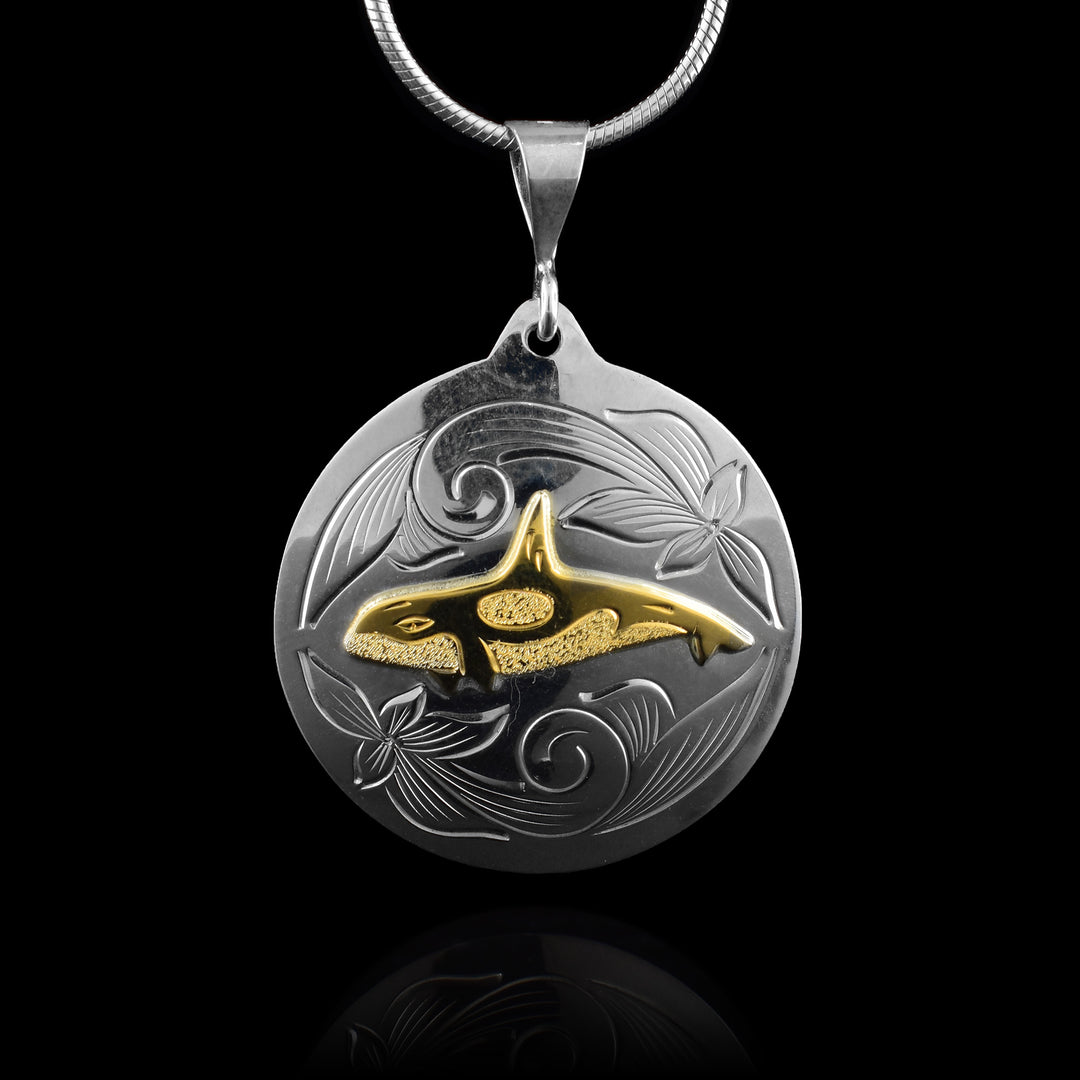 This sterling silver and 14K gold Orca whale pendant has a circle shape and there is an Orca done in gold at a side profile. There are dimpled patterns representing the white spots of the Orca and there are wavy, flower like designs carved not the silver around the whale.