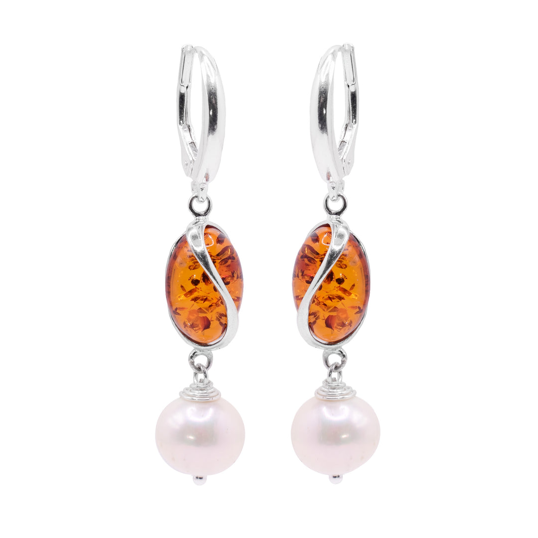 These amber dangle earrings have oval shaped amber beads with a curvy sterling silver designs encasing it. below them, there are sphere shaped pink, freshwater pearl beads that are dangling.