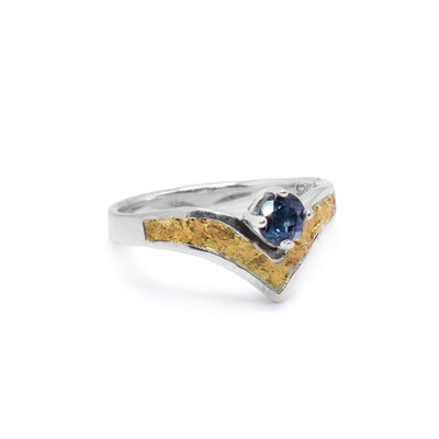 This blue topaz solitaire ring has a thin, sterling silver band that was a V shape in the front. There is a blue topaz gem that is held in the center of the V. The V portion of the top of the band is filled with 22K gold nuggets.